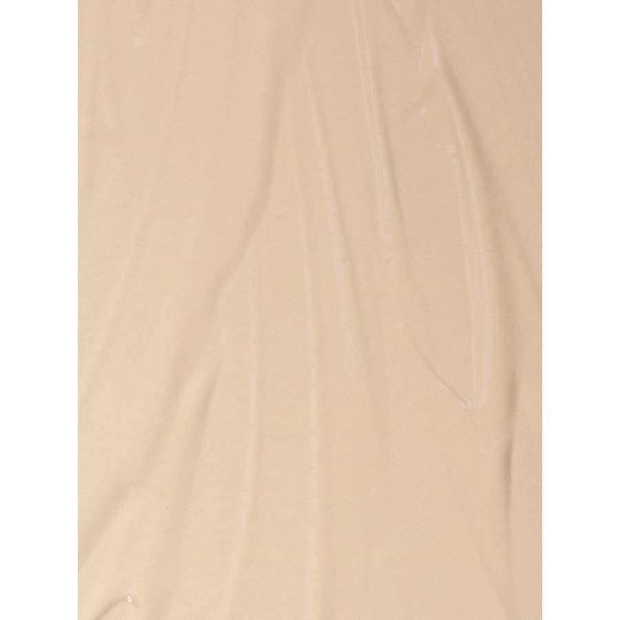 MÁDARA The Concealer, sävy Vanilla; sileä, vaaleanbeige kermainen pinta hienoin juovin ja tekstuurein, muistuttaen ohuelti levitettyä BB-voidetta tai meikkivoidetta; ei näkyvää pakkausta tai etikettiä; matta pinta; ei selkeää muotoa eikä ihmisiä, käsiä tai toimintaa; tasainen valaistus vaalealla taustalla lähikuvassa keskittyen tuotteen tekstuuriin.