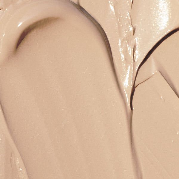 Lähikuva sileästä, kermaisesta beigestä meikkivoiteesta levitettynä kiehkuroina ja kerroksina, jossa näkyy selkeä tekstuuri ja kiiltävä loiste; tuote keskibeige ja kiiltäväpintainen, useita päällekkäisiä sivelyjä näkyvissä; ei pakkausta tai säiliötä näkyvissä; tausta neutraali ja yksivärinen; ei käsiä, ihmisiä, etikettejä tai tekstiä näkyvissä.