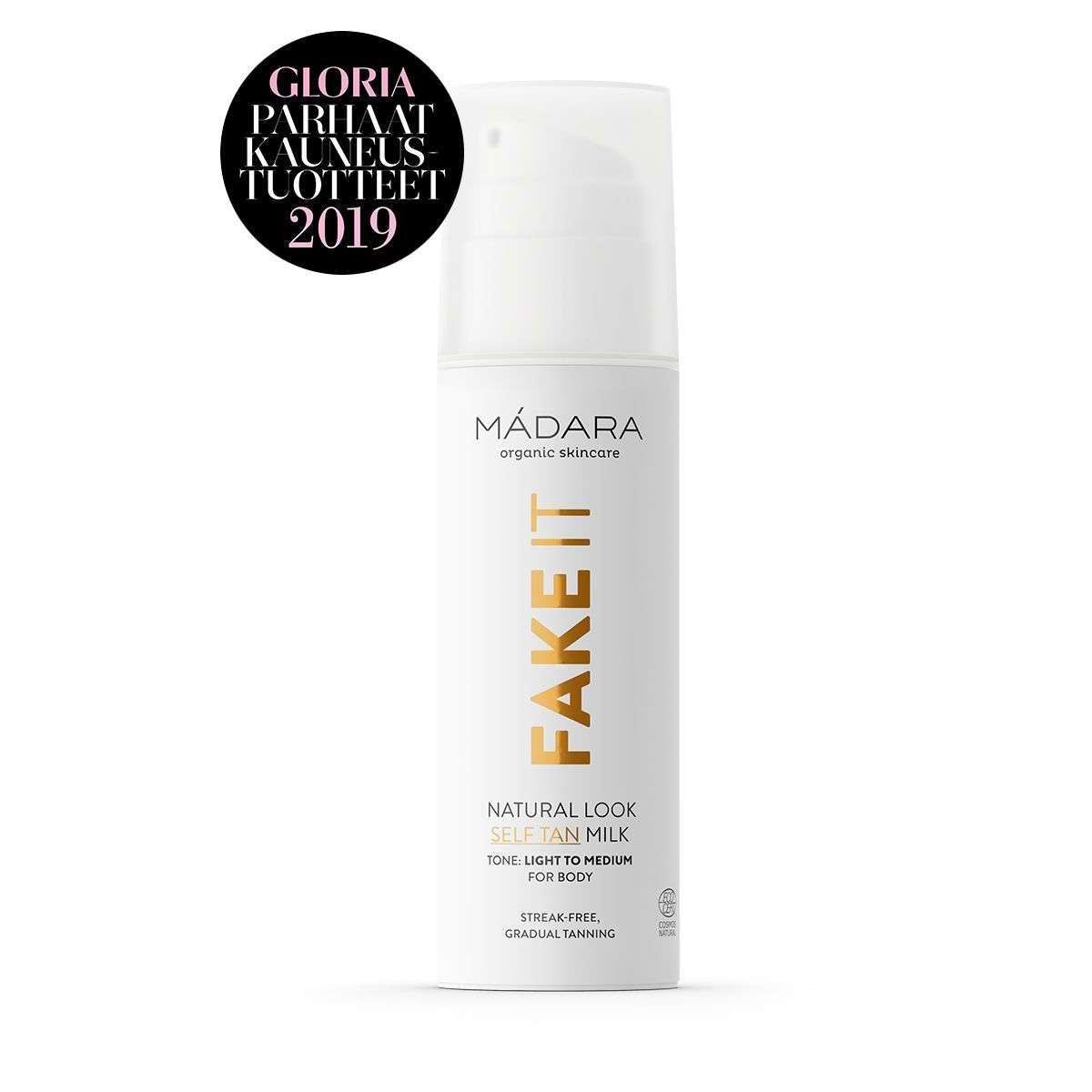 Mádara Fake It Natural Look Self Tan Milk -pullo, valkoinen, kultaisen värisin tekstausvapain tekstein, mattapintainen sylinterimäinen muoto pyöristetyin reunoin ja valkoinen pumppuannostelija; musta pyöreä merkki vasemmassa yläkulmassa, jossa lukee valkoisella "Gloria Parhaat Kauneustuotteet 2019"; tausta yksinkertainen ja siisti; ei ihmisiä tai käsiä näkyvissä.