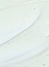 Close-up of a translucent serum with small air bubbles suspended throughout, spread smoothly on a white surface. The serum has a glossy finish and is colorless. No packaging or label text is visible. Background is plain white with no additional objects, people, hands, or actions present in the image.