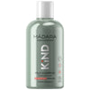 A green plastic bottle of MÁDARA organic skincare KIND mild shampoo has a matte finish and cylindrical shape with a silver cap. The front label features sans-serif white and light gray text, including the brand name, product type, intended users, natural ingredient claim, and visible certification icons. The background is plain white. No people or hands are present in the frame. A green bottle of MÁDARA organic skincare KIND mild shampoo for sensitive skin, enriched with natural ingredients and suitable