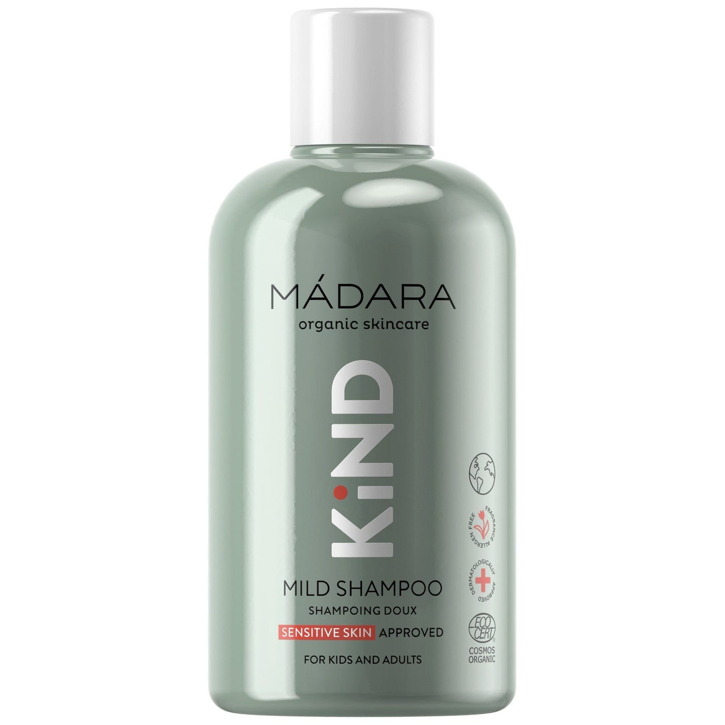 A green plastic bottle of MÁDARA organic skincare KIND mild shampoo has a matte finish and cylindrical shape with a silver cap. The front label features sans-serif white and light gray text, including the brand name, product type, intended users, natural ingredient claim, and visible certification icons. The background is plain white. No people or hands are present in the frame. A green bottle of MÁDARA organic skincare KIND mild shampoo for sensitive skin, enriched with natural ingredients and suitable