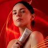 Madara Derma Collagen Night Source Yövoide; henkilö paljain hartioin pitelee MADARA-kosmetiikkatuubia; tuubi sylinterinmuotoinen, metallinhohtoinen ja mattapinnalla; selkeä groteskikirjasin tavaa "MADARA" pakkaukseen; tausta kirkkaan punainen kiemuraisin valaistuin valojuovin; lähikuva keskittyy tuotteeseen ja naisen ylävartaloon, ilmentäen luonnollista kauneutta.