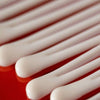 Madara Derma Collagen Night Source Yövoide; lähikuva useista puuvillapuikoista aseteltuna rinnakkaisin viivoin punaiselle pinnalle, esitellen valkoisia puuvillapäitä yksityiskohtaisesti ja korostaen niiden pehmeää imukykyistä tekstuuria; puikot sylinterinmuotoisia muovivarsia mattavalkoisin päin; ei pakkausta tai etikettejä näkyvissä; tausta yhtenäisen punainen, ei ihmisiä tai käsiä kuvassa.