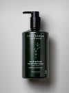 A dark green plastic pump bottle with a matte finish, cylindrical shape, and flat base. The label shows Mádara Wild Woods Moisture Wash with organic skincare, mentions horsetail and absinthium, and states it is suitable for hands and body. The typography is modern sans serif in white. Bottle stands on a smooth light gray background; no people or hands visible.