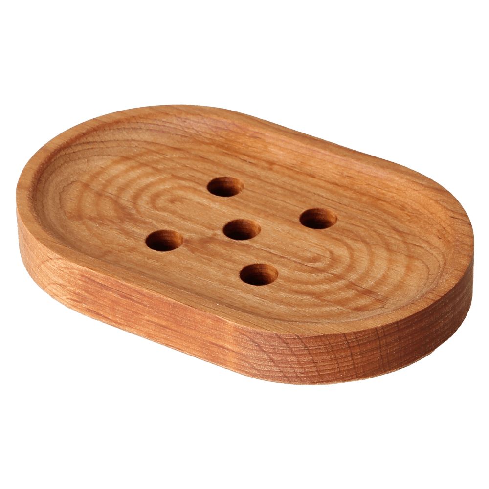 Novapuu Soikea saippua-alunen 130 x 85 mm; puinen soikea saippua-alunen kuudella valumisreiällä kahdessa rivissä, näkyvin puun syykuvioin ja sileä pinta; vaaleanruskea, käsittelemätön tai kevyesti käsitelty mattapinta ilman pakkausta tai etikettiä; ei ihmisiä tai käsiä; valkoinen tausta, lähikuva tuotteesta.