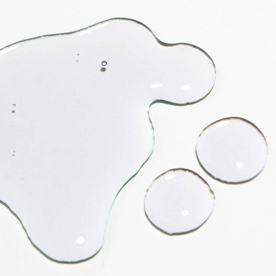 Novexpert HYALURONIC Micellar Water; kirkkaita nestepisaroita valkoisella alustalla, yksi suurempi epäsäännöllinen pisara ja kaksi pienempää pyöreää, sisällä pieniä kuplia; ei näkyvää pakkausta tai etikettitekstiä; tausta tasaisesti valaistu, kuvattu suoraan ylhäältä; ei ihmisiä tai käsiä.