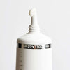 Novexpert PRO-COLLAGEN Expert Anti-Aging Fluid; lähikuva valkoisesta tuubista, jossa osittain näkyvissä teksti "PROCOLLAGEN"; suuttimesta tulee pieni määrä hoitovoidetta valkoiselle taustalle; tuubi sileä ja kiiltäväpintainen, yksinkertainen groteskikirjasin; ei käsiä tai ihmisiä kuvassa.