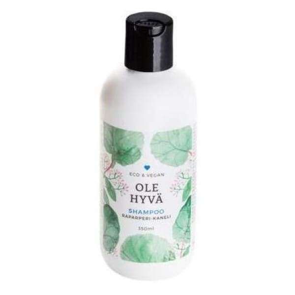 Ole Hyvä Shampoo Raparperi-Kaneli -pullo, 350 ml; valkoinen, mattapintainen ja sylinterimäinen pullo mustalla korkilla; etiketissä vihreitä lehtigrafiikoita ja selkeää tekstausvapaata tekstiä, merkinnät "Eco & Vegan" ja tuoksutiedot; kuvattu yksiväristä taustaa vasten, ei ihmisiä tai käsiä näkyvissä.