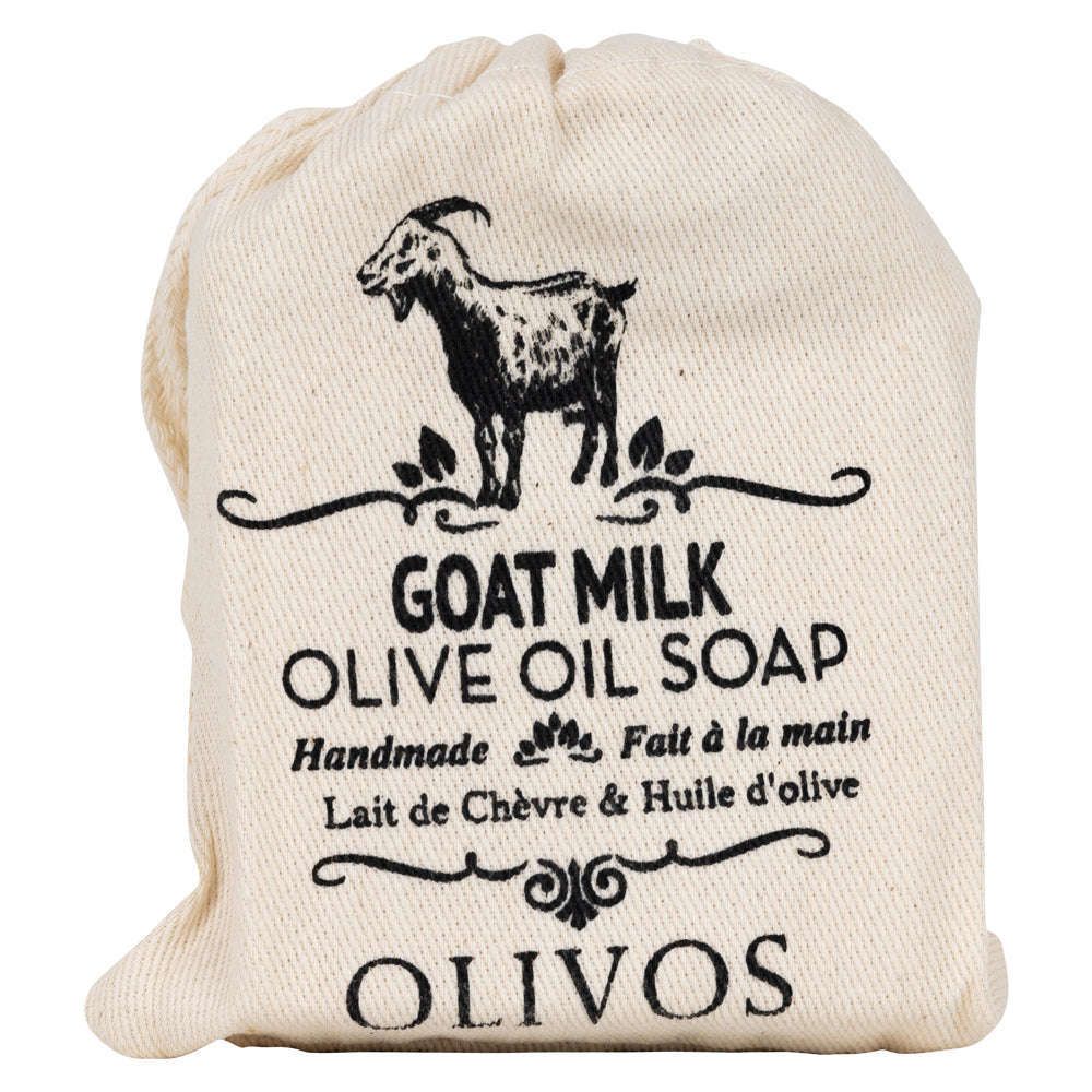 Olivos Vuohenmaitosaippua; kangaspussi tekstillä "Goat Milk Olive Oil Soap" ja vuohen kuvitus; teksti korostaa käsintehtyä Olivos-tuotetta englanniksi ja ranskaksi, mainiten vuohenmaidon ja oliiviöljyn ravitsevan yhdistelmän; pussi luonnonvalkoinen mustalla painetuin tekstein serifi- ja groteskikirjasimin; valkoinen tausta, ylhäältä kuvattu, ei ihmisiä tai käsiä.