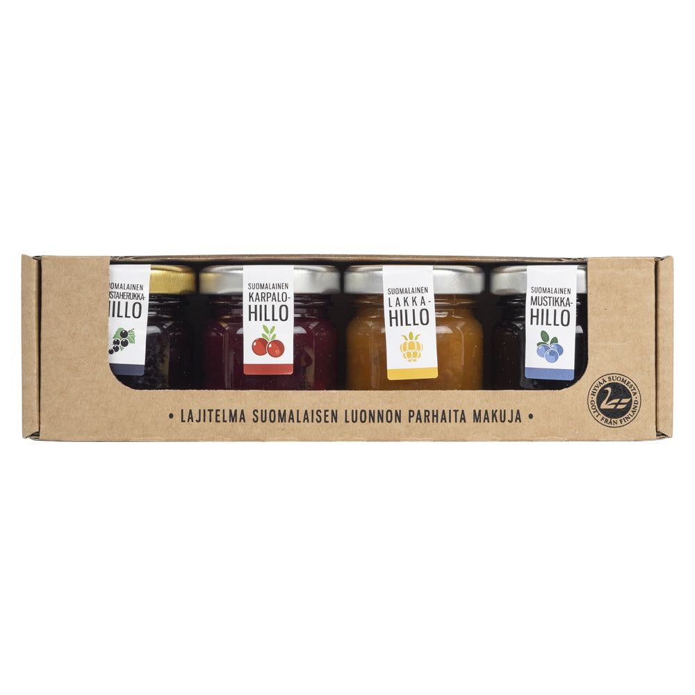 A set of four Finnish jam jars in a cardboard box, each labeled with different berry flavors and vibrant colors—green, red, orange, and blue. Authentic Finnish text appears on both the box and jar labels. The jars are clear glass with metallic lids, cylindrical in shape. Labels have bold printed Finnish words and simple graphics. Cardboard packaging has a matte finish. Jars are upright in the box against a neutral background; no people or hands visible.