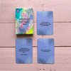 A set of Finnish emotion cards on a pink wooden surface, featuring expressive text and delicate leaf illustrations. One rectangular card box and three matte finish cards are arranged side by side. Cards are white with black sans-serif typography and subtle gray leaf patterns. No people or hands present in the shot.