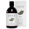 A bottle of SEES No1 Cedar & Orange Shampoo is shown next to its box. The cylindrical bottle is matte white with a black screw cap, and the rectangular box is also matte white with black text. Both display sans-serif typography. Label text includes “No1,” “Cedar & Orange,” and reference to biodegradable formula, strengthening, nurturing, and made in Finland. The background is plain and light-colored with no people or hands visible. Shot is front-facing at eye level.