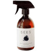 A brown plastic spray bottle with a matte finish. The bottle is cylindrical with curved shoulders and a black trigger spray nozzle. The label reads: SEES Multi-Surface Cleaner with bergamot and lemon, described as ecological and plant-based. Minimalist black circular design on label. Plain background, no people or props in the image.