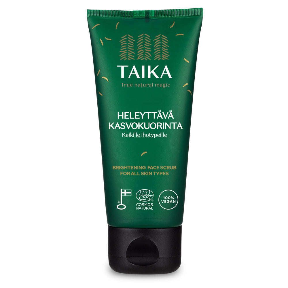 A green squeeze tube with a matte finish labeled Taika Brightening Face Scrub for all skin types, with white and yellow sans-serif text, eco and vegan symbols, and a black plastic flip-top cap. The product is photographed upright on a plain white background. No people or hands visible in the shot.