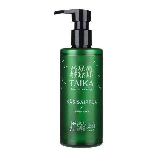 Taika Käsisaippua; vihreä Taika-käsisaippuan pumppupullo mattapinnalla; pullo lieriömäinen mustalla muovipumpulla; etiketissä valkoista tekstiä siistillä groteskifontilla, tyylitellyt puukuvitukset ja luonnonteema; tuotetyyppi ja brändinimi luettavissa etuosassa; ei ihmisiä tai käsiä; studiotausta, tasaisesti valaistu kuva.