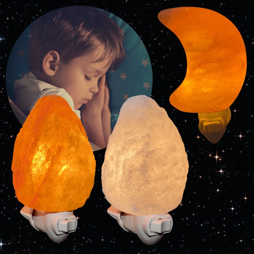 A sleeping child is nestled among three night lights: one shaped like a crescent moon with a matte finish, and two rock-shaped lights with smooth surfaces, glowing in orange and white. No visible packaging or label text. The background features illustrated stars and dark blue coloration resembling a starry night. The image is composed as a close-up scene.
