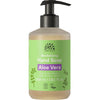 Urtekram Aloe Vera Käsisaippua; Urtekram Revitalizing Hand Soap with Aloe Vera -pumppupullo, käytännöllinen koko 300 ml (10,1 fl. oz.); pullo lieriömäinen, mattavalkoinen runko ja musta muovinen pumppuannostelija; etuosassa suorakulmainen vihreä etiketti valkoisin groteskitekstein sekä luomu- ja vegaanisertifiointisymbolein; kuvassa vain tuote vaalealla, kevyellä taustalla.