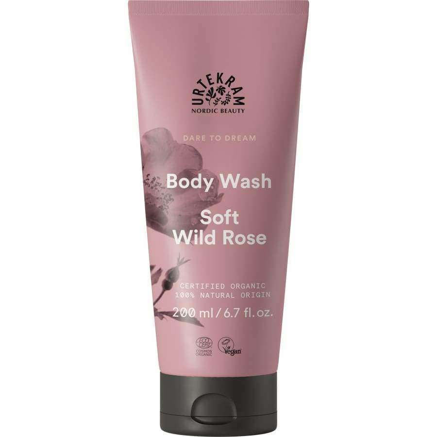 Urtekram Dare to Dream Soft Wild Rose Suihkusaippua; vaaleanpunainen, mattapintainen muovituubi tekstillä "Urtekram Nordic Beauty Body Wash, Soft Wild Rose, 200 ml", keskitettynä kuvaan; etuosassa valkoisia kukkakuvituksia ja vegaani- sekä luomusertifiointisymboleita; tuotetyyppi ja tilavuus painettu selkeällä groteskifontilla; ei ihmisiä tai käsiä; tausta yksinkertainen ja neutraali.