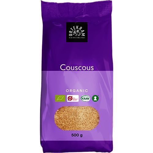 500 g:n pussi Urtekramin luomu-täysjyväcouscousia violetissa pakkauksessa, jossa näkyy luomustandardien sertifikaattilogoja. Pakkaus on mattapintainen ja suorakulmainen, uudelleensuljettavalla yläreunalla. Valkoinen pääteviivaton teksti näyttää tuote- ja brändinimet. Useita logoja näkyy alaosan lähellä etupuolta. Tausta on neutraali, eristetty tuotekuva ilman ihmisiä tai rekvisiittaa.
