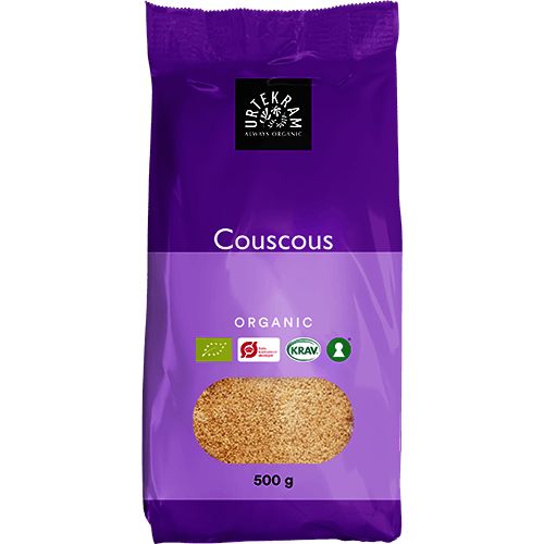 500 g:n pussi Urtekramin luomu-täysjyväcouscousia violetissa pakkauksessa, jossa näkyy luomustandardien sertifikaattilogoja. Pakkaus on mattapintainen ja suorakulmainen, uudelleensuljettavalla yläreunalla. Valkoinen pääteviivaton teksti näyttää tuote- ja brändinimet. Useita logoja näkyy alaosan lähellä etupuolta. Tausta on neutraali, eristetty tuotekuva ilman ihmisiä tai rekvisiittaa.