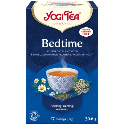 YogiTea Luomu Bedtime -teepakkaus; kuvassa teekuppi ja kamomillankukkia; suorakulmainen pahvipakkaus mattapinnalla, pääväri sininen ja keltainen; luettavassa etiketissä teksti "Ayurvedic blend", "naturally caffeine free", "17 teabags"; serif-fontti tuotenimessä, tekstausvapaata fonttia yksityiskohdissa; tausta valkoinen; ei ihmisiä tai käsiä näkyvissä; kuva otettu edestä silmän tasolta.