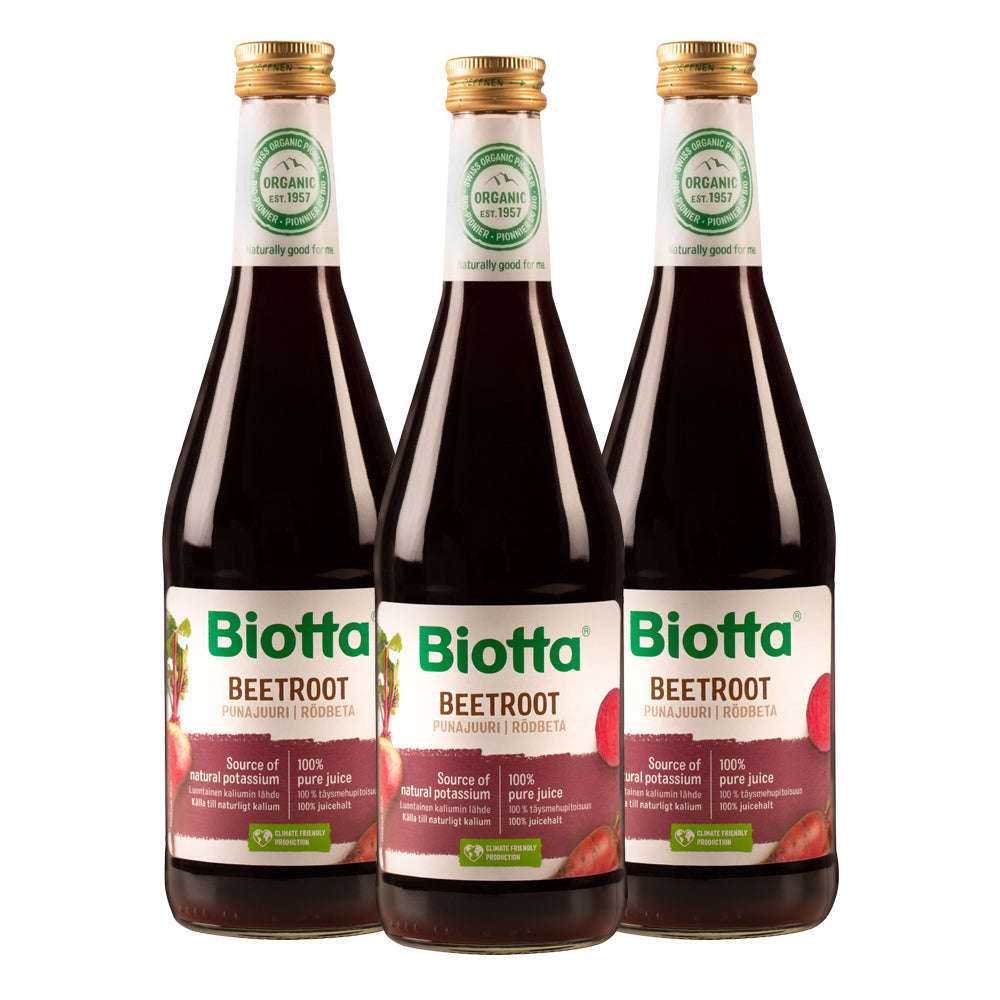 Biotta Luomu Punajuuritäysmehu 3-pack; kolme kirkasta, lieriön muotoista ja kiiltäväpintaista lasipulloa kultaisin korkein, sisällä tummanpunaista mehua; etiketeissä punajuurikuvia, tuotetietoja groteskitekstillä ja luomusertifiointilogo yläreunassa; valkoinen tausta.