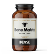 DENSE Bone Matrix; ruskea pillerimpullo tekstillä "Bone Matrix Grass-Fed" ja lehmänpäälogolla, 180 kapselia à 1000 mg; merkitty 100-prosenttisesti eläinperäiseksi laiduntuotannosta; lieriön muotoinen muovipullo mattapintaisena kierrekorkilla; lihavoitua valkoista ja vihreää groteskitekstiä tummalla pohjalla; valkoinen tausta, ei ihmisiä tai tarvikkeita.
