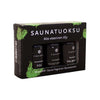 Emendo Saunatuoksu 3-pack; kolme Emendo-saunatuoksuöljypulloa pakattuna mustaan rasiaan tekstillä SAUNATUOKSU, vihrein siveltimenvetokuvioin ja valkoisin suomenkielisin tekstein perinteisen saunakulttuurin inspiroimana; pullot lieriömäisiä valkoisin korkein, tummansävyistä lasia, etiketti edessä näyttää tuotenimen; rasia mattapintainen; ei ihmisiä tai käsiä; tausta yhtenäisen valkoinen, kuva otettu suoraan edestä tuotteen tasolta.