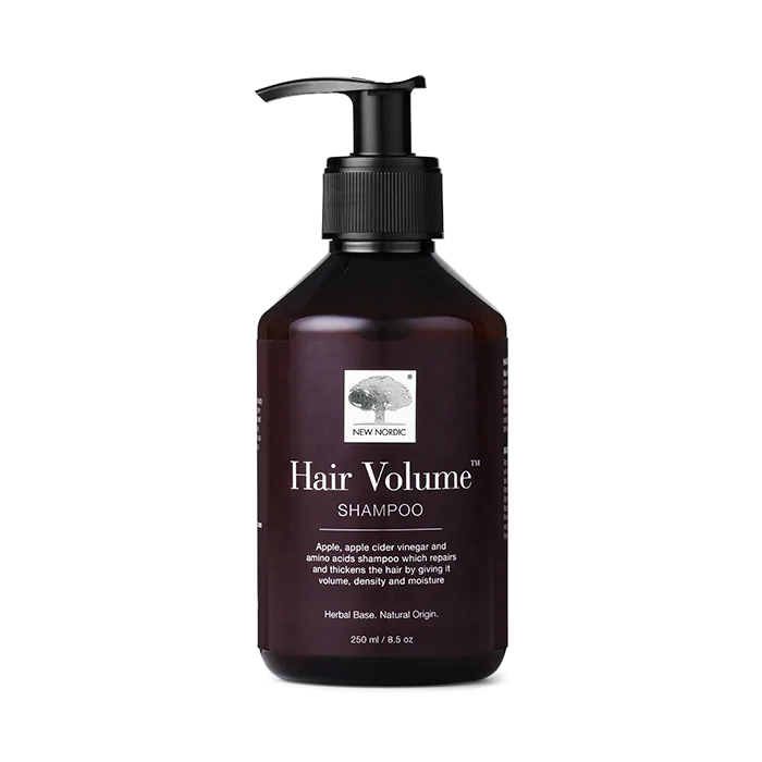 Hair Volume Shampoo; tumma, lieriön muotoinen ja kiiltäväpintainen pumppupullo New Nordic -tuotemerkillä, tekstissä mainitaan omenauute ja tarkempia tuotetietoja pienen logon alla; selkeä groteskitypografia; sisältö 250 ml; neutraali tausta.