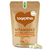 Together Health Vitamin K2; ruskea uudelleensuljettava pussi tekstillä "Together Vitamin K2 Natural MK7 Form from fermented chickpeas", kuvituksena kikherne, sisältää 30 kasviskapselia; kaksi valkoista kasviskapselia esillä pussin edessä; pussi mattapintainen ja suorakulmainen pyöristetyin reunoin; teksti selkeällä groteskikirjasimella valkoisena ja keltaisena; yksivärinen tausta, ei ihmisiä kuvassa.