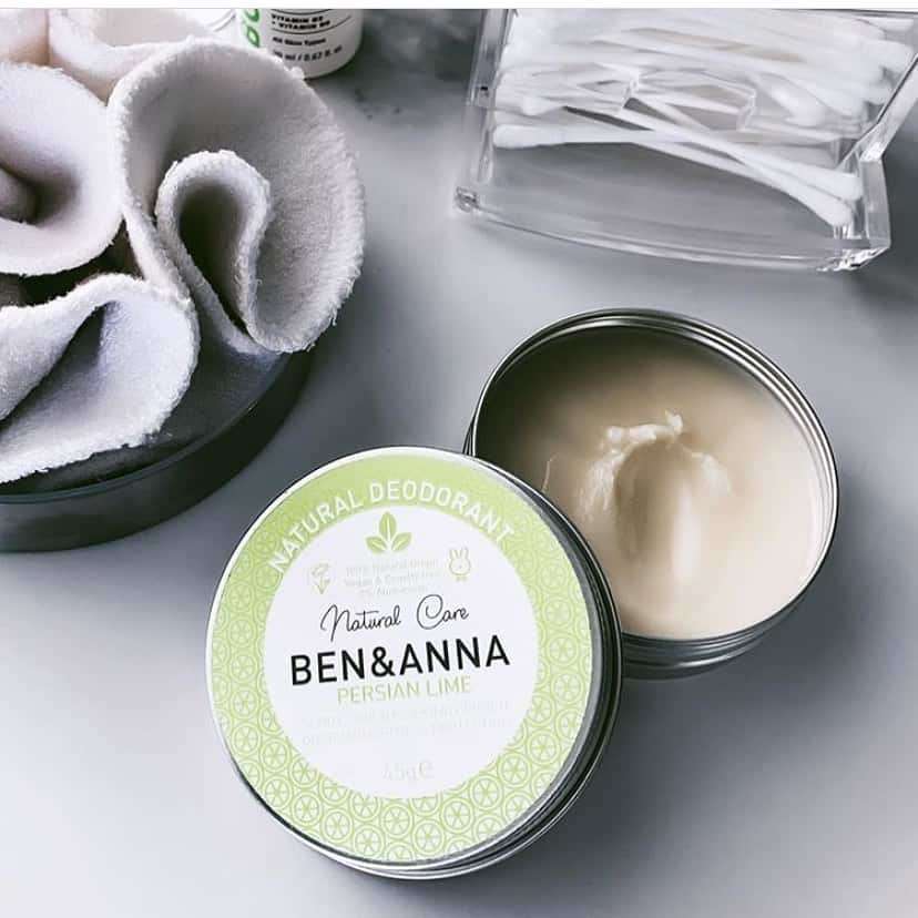 Ben & Anna Voidedeodorantti Persian Lime; avoin Ben & Anna Persian Lime -luonnollisen deodoranttivoiteen rasia pöydällä, vieressä kulho kestokäyttöisiä puuvillalappuja ja pakkaus biohajoavia vanupuikkoja; rasia pyöreä, metallinen, vihreällä etiketillä ja tuotenimi valkoisin kirjaimin; kulho valkoista keramiikkaa; vanupuikkopakkaus suorakulmainen pahvilaatikko niukalla tekstillä; kaikki sileällä pöytätasolla, ei ihmisiä tai käsiä laajassa kuvassa.