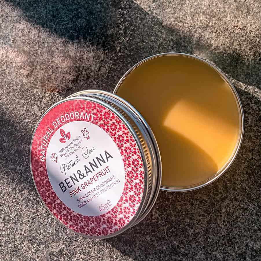 Ben & Anna Voidedeodorantti Pink Grapefruit; pyöreä peltirasia Ben & Anna Natural Care Pink Grapefruit -deodoranttia avoinna kivipinnalla, sisällä sileää, kellertävää voidetta; rasiassa painettua etikettitekstiä selkeällä groteskifontilla ja mattapinta; auringonvalo korostaa voiteen tekstuuria; ei ihmisiä tai käsiä kuvassa.