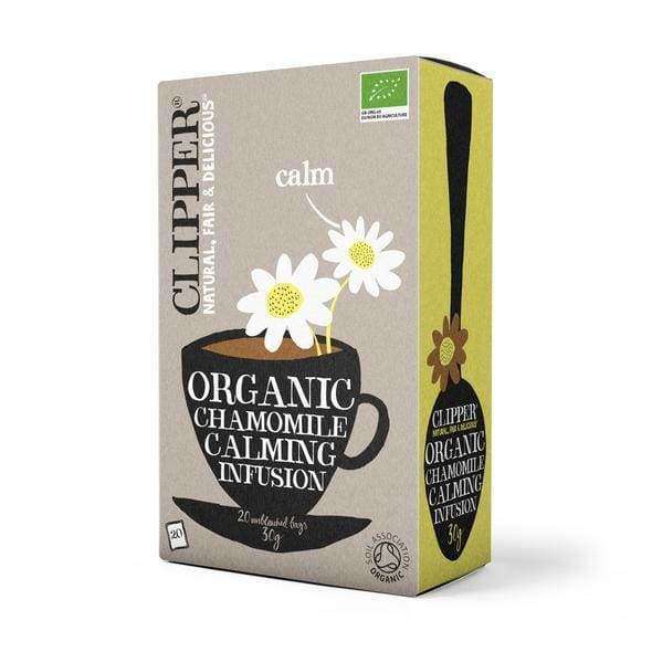Clipper Organic Chamomile Calming Infusion -tee; kuvituksena kaksi päivänkakkaraa mustassa teekupissa; suorakulmainen rasia mattapintaisesta pahvista, vaaleankeltainen tausta, lihavoitua groteskitekstiä ja hienovaraisia käsialaelementtejä; luettavissa maininnat "organic" ja "fair"; ei ihmisiä tai käsiä; kuvattu vaalealla taustalla.