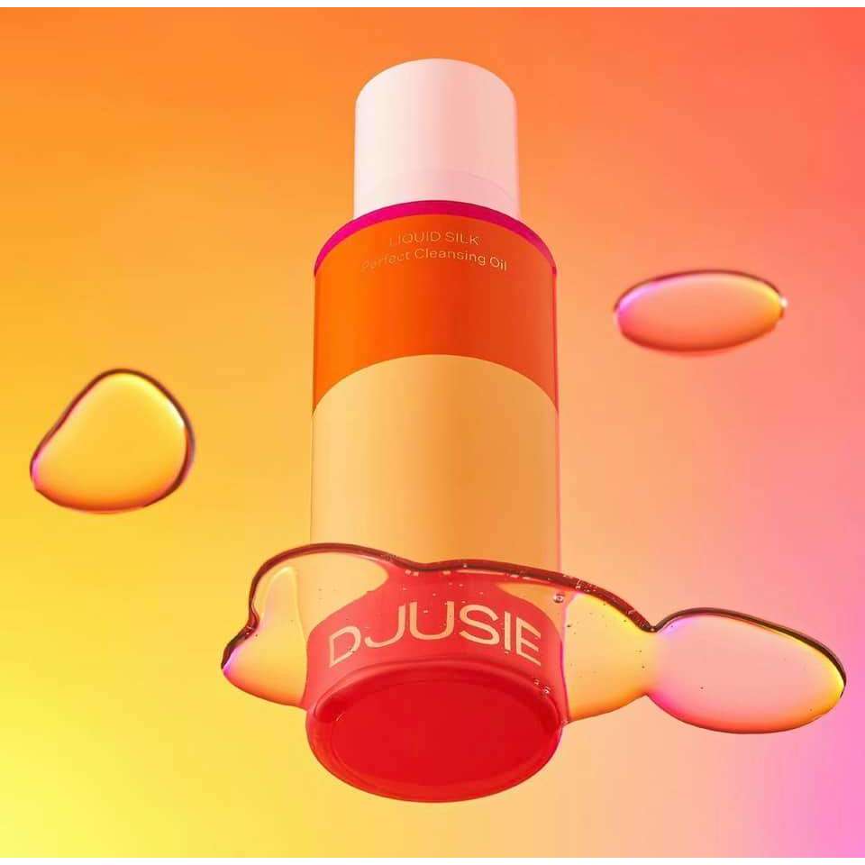 Djusie Liquid Silk Perfect Cleansing Puhdistusöljy; pullo DJUSIE Liquid Silk -puhdistusgeeliä leijuen kiiltävien nestepisaroiden ympäröimänä värikkään liukuväritaustan edessä, korostaen eloisaa ja leikkisää tunnelmaa; pullo läpikuultava kevyen pinkin sävyisenä pumppuannostelijalla; teksti "DJUSIE" ja "Liquid Silk" lihavoiduin nykyaikaisin groteskikirjaimin etuetiketissä; ei ihmisiä tai käsiä kuvassa.