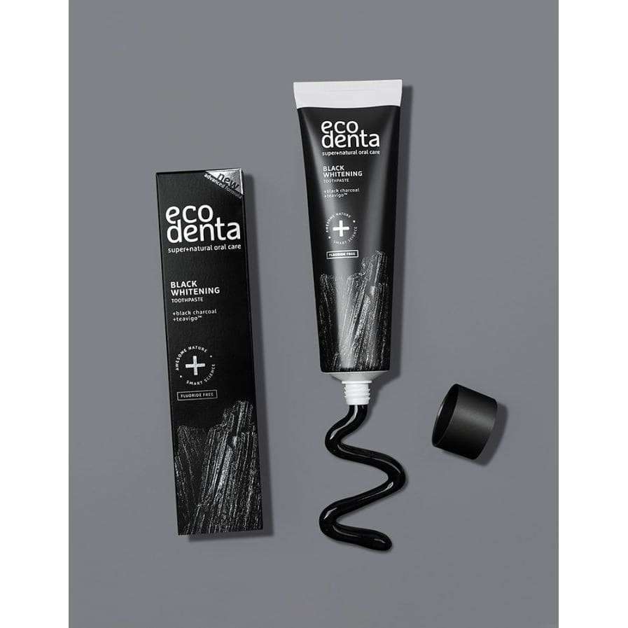 Ecodenta Black Whitening -valkaiseva hammastahna; putkilo ilman korkkia, mustaa aktiivihiilitahnaa puristettuna ulos, rasia vieressä harmaalla taustalla; putkilo ja rasia mattamustia valkoisin groteskitekstein; etiketissä suurin kirjaimin "Ecodenta Black Whitening"; suorakulmainen rasia pystyssä lieriömäisen putkilon vieressä; ei ihmisiä tai käsiä; pehmeästi valaistu studiokuva.
