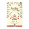 English Tea Shop Luomu Happy Me -teepakkaus; suorakulmainen ja mattapintainen rasia, pääväri turkoosinsininen, kuvituksena monivärisiä kukka- ja lehtikuvioita; valkoinen päätekirjasin, jossa käsialamaisia korostuksia; etiketti mainitsee 20 biohajoavaa teepussia sekä sitruunaruohon, appelsiinin, inkiväärin ja kanelin; kuvattu valkoista taustaa vasten, ei ihmisiä näkyvissä.