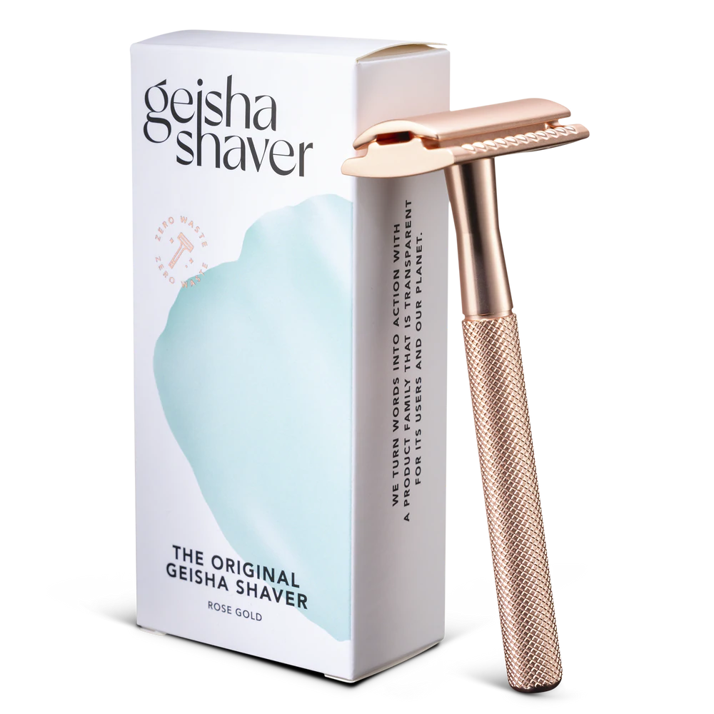 The Original Geisha Shaver -parranajokone; ruusukultainen partakone pystyssä pakkauksensa vieressä; partakoneen pinta kiiltävä metallinen, kahva perinteisen lieriömäinen; suorakulmainen rasia pääosin valkoinen, vaaleansinisin ja hopeanvärisin yksityiskohdin, groteskitekstiä; molemmat esineet vaalealla, tasaisella taustalla; ei ihmisiä tai käsiä.