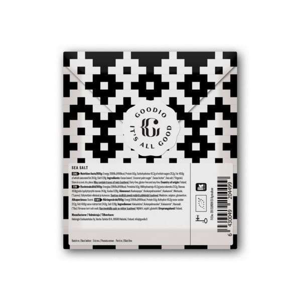 Goodio-suklaapatukan käärepaperi, musta ja valkoinen geometrinen kuviointi, pyöreä logo tekstillä "It's All Good" sekä merisuolamaun ja ainesosien merkintä pakkauksen alaosassa; käärepaperi mattapintainen, suorakulmainen muoto, lohkomaista tekstausvapaata typografiaa; kuva näyttää vain pakatun patukan yhtenäisellä taustalla tasokuvana; ei ihmisiä tai toimintaa näkyvissä.