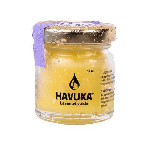 Havuka Laventelivoide, 40 ml; pieni lasipurkki kultaisella kierrekannella; lasin pinnalla näkyy vesipisaroita; violetti nauha sidottu tiukasti kannen ympärille; purkki täynnä keltaista voidetta, valkoisessa etiketissä lukee "40 ml"; ei ihmisiä tai käsiä; vaalea tausta.