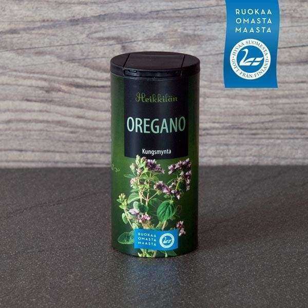 Heikkilän Oregano -purkki harmaalla työtasolla; kirkas muovipurkki mustalla mattapintaisella kierrekannella, vihreä etiketti oreganokukka- ja lehtikuvituksella, suomalainen sertifiointimerkki tuotenimen vieressä