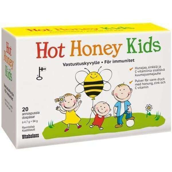 Hot Honey Kids -pakkaus; suorakulmainen, mattapintainen pahvipakkaus pääosin keltaisena punaisin yksityiskohdin; etiketissä sarjakuvamaisia lapsihahmoja ja mehiläinen sekä tekstiä immuniteetin ja hyvinvoinnin tuesta; lihavoitu merkki yläosassa, alaosassa ainesosaluettelo ja maininta 20 annospussista; kuvattu valkoista studiotaustaa vasten kokonaan kuvassa, ei ihmisiä tai käsiä näkyvissä.