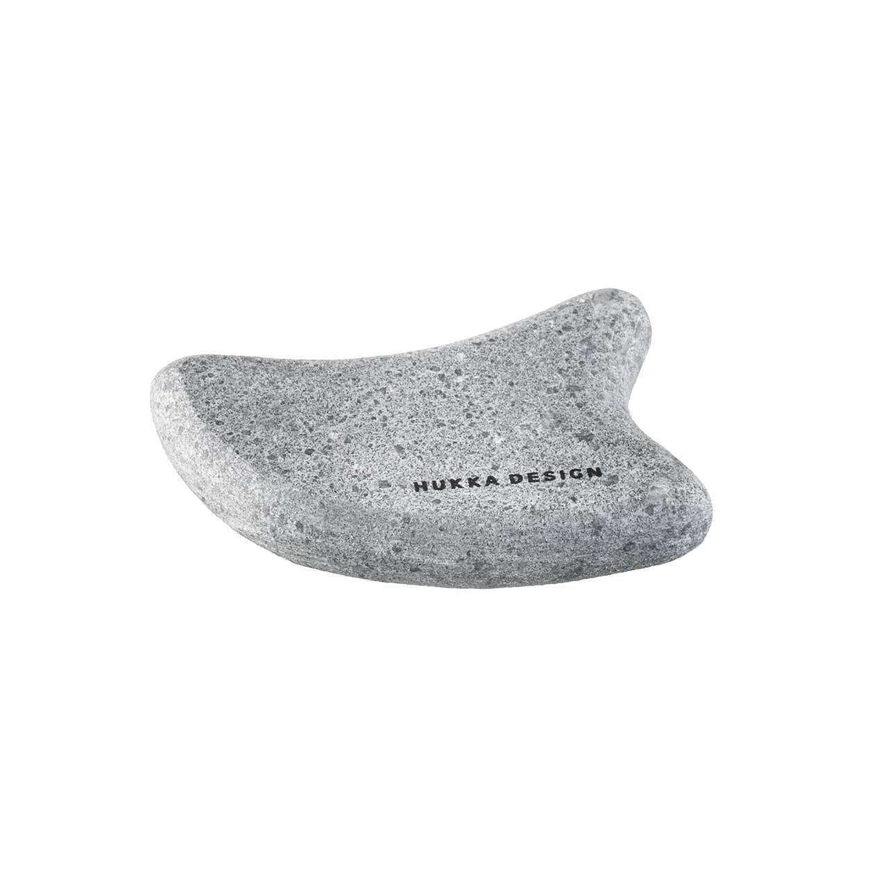 NUKKA DESIGN -guasha, kissan muotoinen; sileä, harmaa mattapintainen kivi kaarevalla, ergonomisella rungolla ja kahdella terävällä korvamaisella ulokkeella; brändinimi painettu selkeällä mustalla groteskitekstillä; ei näkyvää pakkausta; vaalea tausta, ei ihmisiä tai käsiä; studiokuva.
