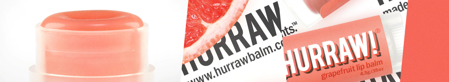 Lähikuva vaaleanpunaisesta huulivoidepuikosta ja greippiviipaleesta, tuubissa lihavoitu "HURRAW!" valkoisella ja punaisella; luonnonvalkoinen mattapintainen puikko