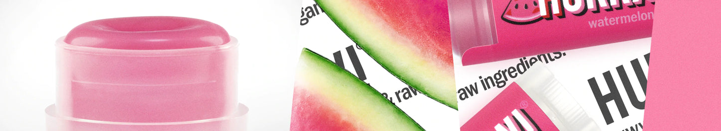 Hurraw! Huulivoide Vesimeloni; lähikuva vaaleanpunaisesta huulivoidepuikosta, vesimelonipaloista ja vaaleanpunaisesta pakkauksesta tekstillä "watermelon", osittain näkyvissä sanoja "raw ingredients" ja "HUM"; huulivoide sylinterinmuotoinen mattapinnalla; pakkaus suorakulmainen, kiiltäväpintainen ja vaaleanpunainen; typografia lihavoitua groteskityyliä; pelkistetty valkoinen tausta, ei ihmisiä tai käsiä kuvassa.