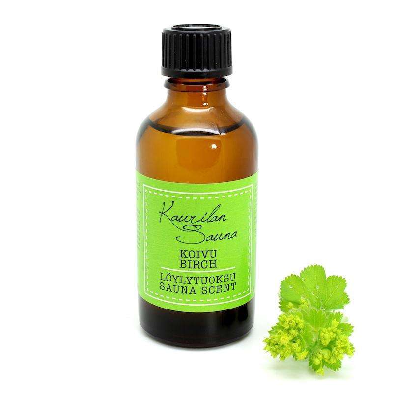 Kaurilan Sauna Löylytuoksu Koivu; ruskea lasipullo mustalla korkilla ja vihreällä etiketillä tekstillä "Koivulan Sauna Birch Sauna Scent", vieressä pieni koivunlehtivihreä kasvi; pullo sylinterinmuotoinen mattapintaisena, korkki pyöreä ja sileä; etiketin teksti valkoisella groteskikirjasimella; valkoinen tausta, ei ihmisiä, käsiä tai toimintaa kuvassa.