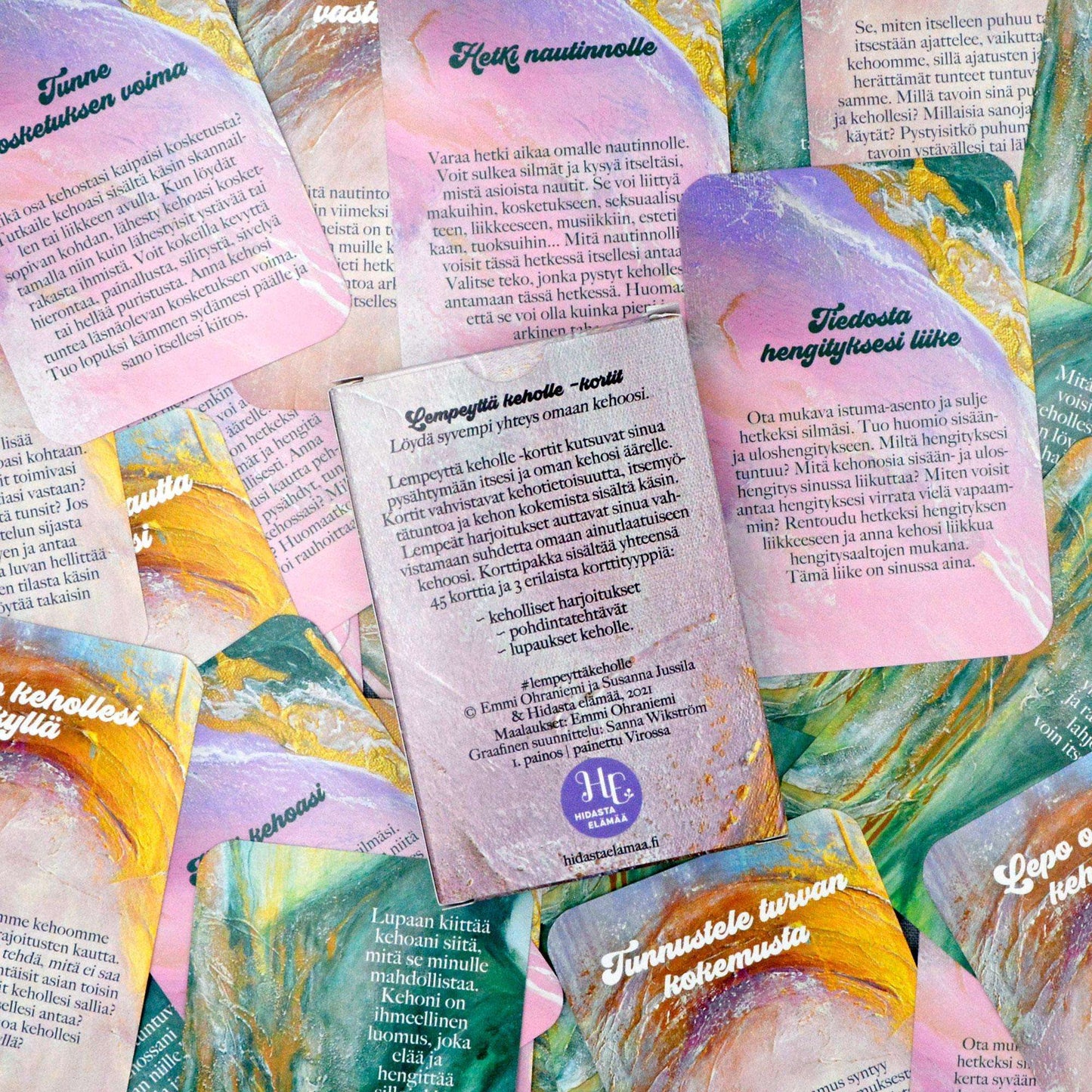 Hidasta Elämää Lempeyttä keholle kortit; hajallaan aseteltuja värikkäitä suomenkielisiä kortteja tekstein, pastellisävyisin siveltimenvetokuvioin pinkin, vihreän, oranssin ja violetin sävyissä vaalealla taustalla; kortit suorakulmaisia mattapintaisin pyöristetyin kulmin; keskikortti pystysuuntainen, teksti selkeällä groteskikirjasimella; ei pakkausta tai ihmisiä kuvassa; ylhäältä kuvattu asetelma erikoisin suomenkielisin lausein.