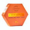 LUONKOS Celebrate Sparkling Body Cake, teksti "Handmade with love"; oranssi kuusikulmainen rasia kultaisin korostuksin ja ylellisin kimalluksin; sivut mattapintaiset, kultaiset metalliset yksityiskohdat; pääteksti lihavoidulla groteskifontilla, "Handmade with love" käsialatyylisellä fontilla; tuote kuvattu vaalealla taustalla, ei ihmisiä tai esineitä.