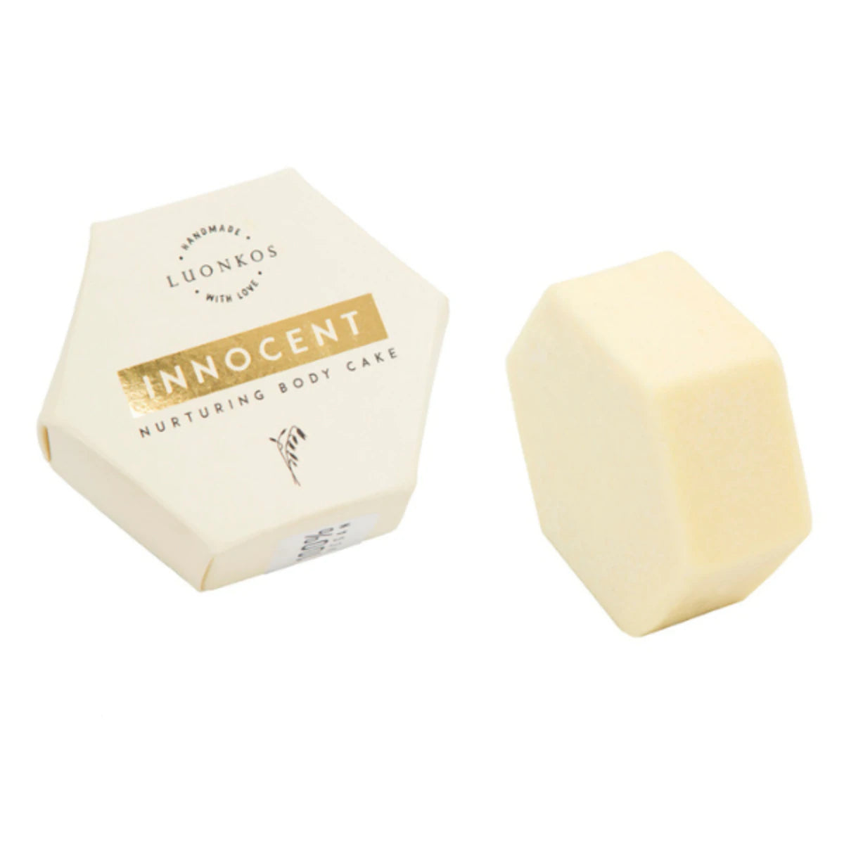 Luonkos Innocent Nurturing Body Cake; kuusikulmainen valkoinen rasia vaalean, mattapintaisen kuusikulmaisen kappaleen vieressä; rasia kartonkia kultafoliolla ja mustalla groteskitekstillä etupaneelissa; molemmat aseteltu tasaiselle, neutraalille pinnalle, ei näkyviä ihmisiä tai käsiä; kuva otettu ylhäältäpäin näyttäen vain tuotteet.