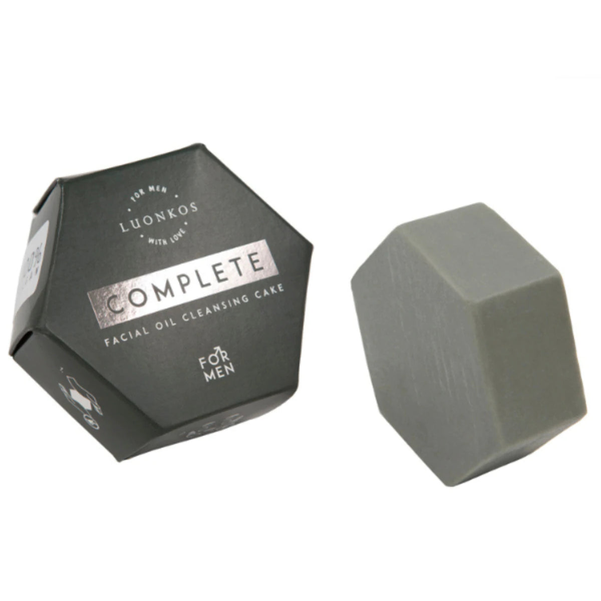 Luonkos Complete Facial Oil Cleansing Cake For Men; tumma kuusikulmainen rasia harmaan, monikulmaisen kiinteän palan vieressä; rasiassa kultaista ja valkoista groteskitekstiä mattapinnalla; molemmat aseteltu valkoiselle taustalle ilman muita näkyviä esineitä tai tekstuureja; ei ihmisiä tai käsiä; yksinkertainen tuotekuva viistosti ylhäältä.